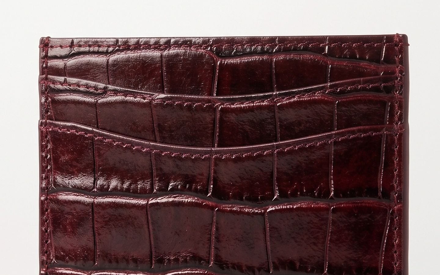 Les trois fentes avant du porte-cartes en cuir de veau embossé croco bordeaux, finition vernie.