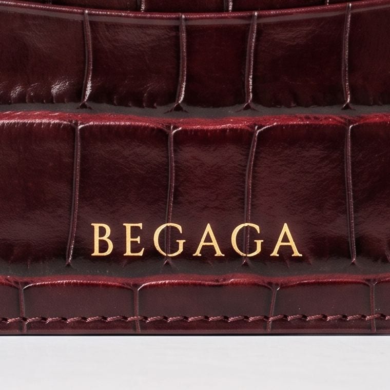Macro du logotype BEGAGA marqué à la feuille d'or sur le cuir embossé croco bordeaux.